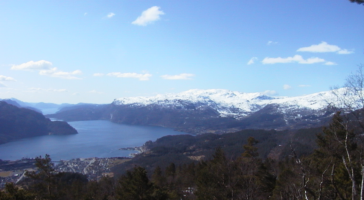 Utsikt over hustak mot Saudafjorden, med bratte fjell på begge sider av vannet.